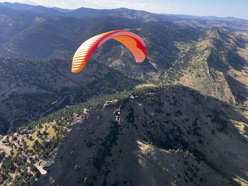 An orange paraglider above forested ridges.