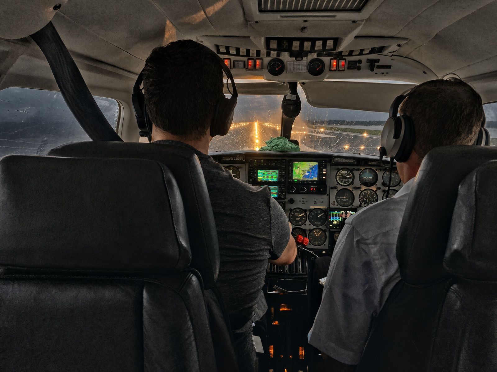 Two pilots in a light twin on approach to a lit runway in the rain.